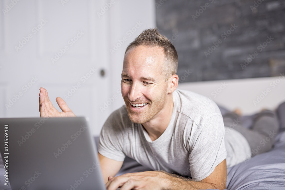 Serious casual young man using laptop in bed at home Serious casual young man using laptop in bed at home