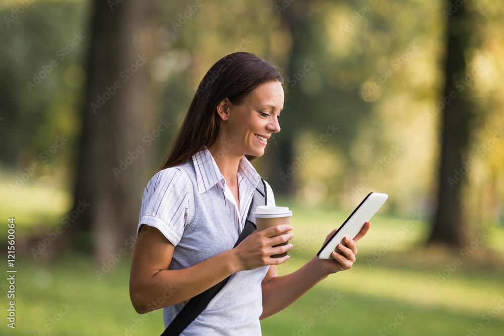 Beautiful businesswoman is drinking coffee and using digital tablet while resting from work at the park.
