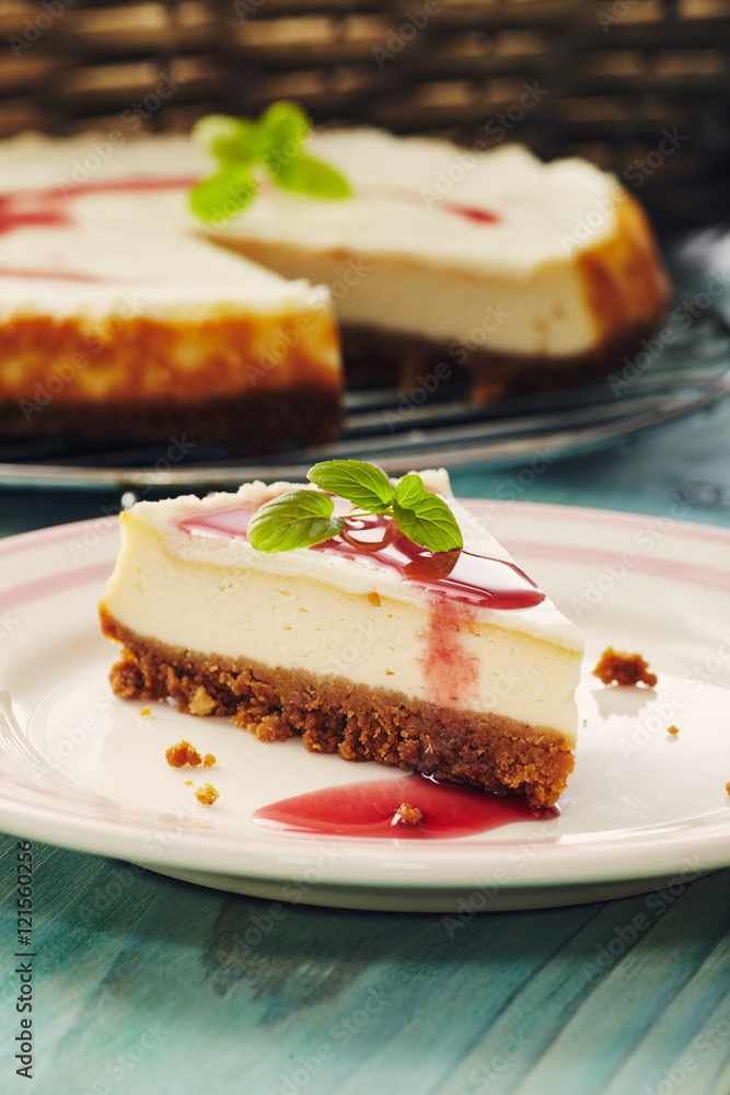 new york cheesecake with cherry sauce on a plate on a blue wooden table, full cake in background new york cheesecake with cherry sauce on a plate on a blue wooden table, full cake in background