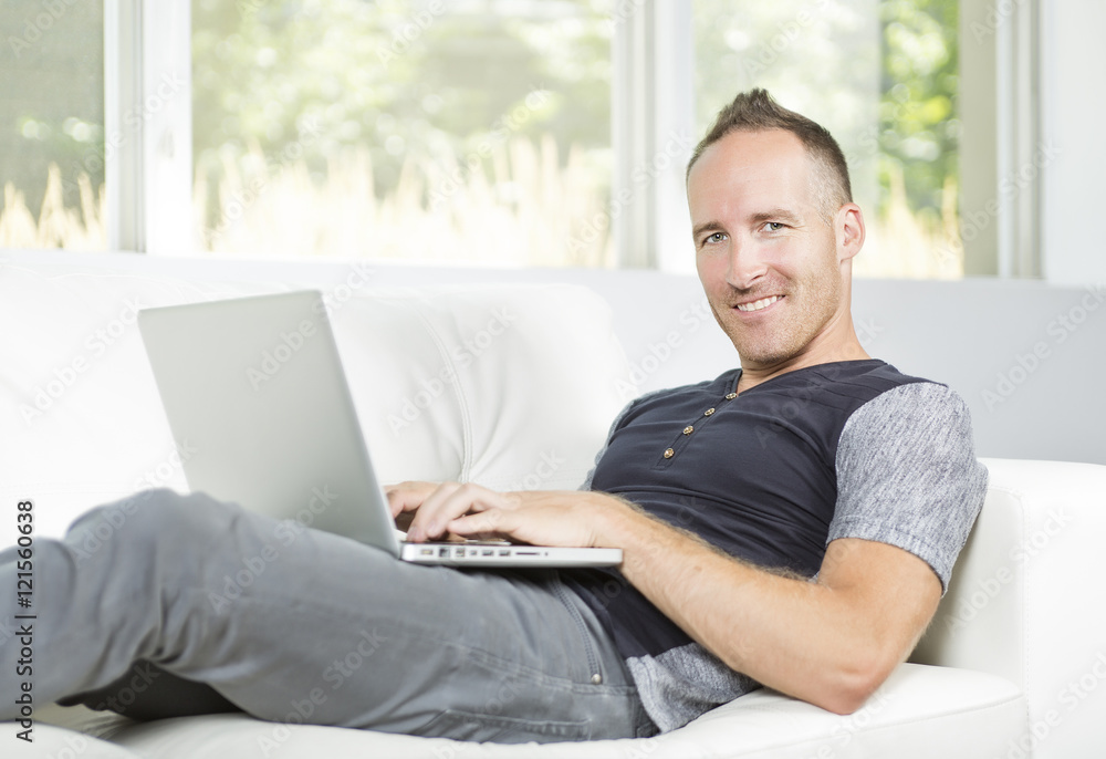 Front view of a handsome man using laptop sitting on couch at home Front view of a handsome man using laptop sitting on couch at home