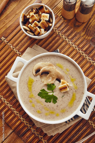 Mushroom cream soup on a table  with bread  garlic  and raw mushrooms on a white chopping board. Salt and Pepper on the table..