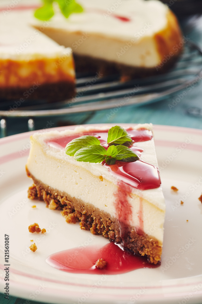 new york cheesecake with cherry sauce on a plate on a blue wooden table, full cake in background new york cheesecake with cherry sauce on a plate on a blue wooden table, full cake in background