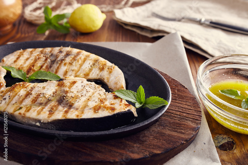 Fotografiet grilled swordfish slices in a cast iron pan on a wooden table, garnished with mi