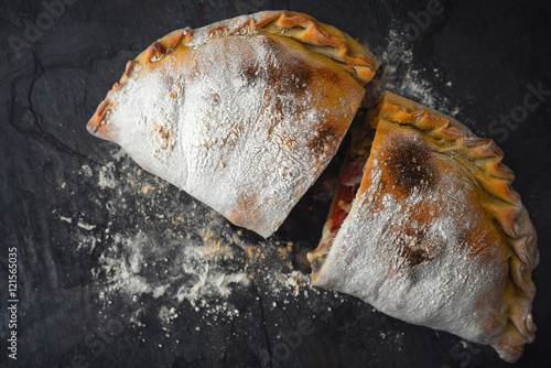 Sliced calzone with flour on the dark stone background top view photo