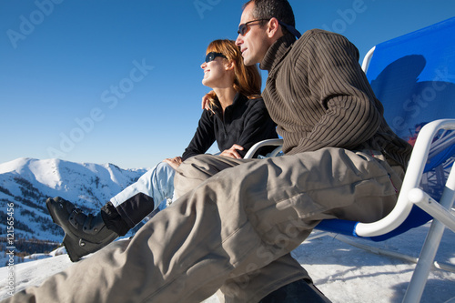 couple souriant assis dans des transats dans la neige