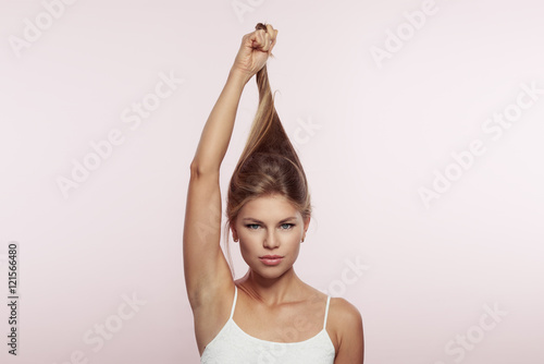 Studio portrait of gorgeous female stretching her long healthy shiny hair over pink background. Concept of hair treatment, stroking and health. 