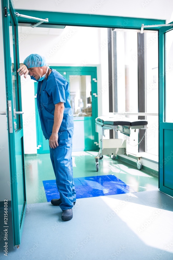 Sad surgeon leaning against the glass door Sad surgeon leaning against the glass door