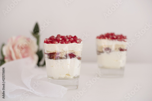 Homemade layered dessert with mascarpone, chocolate, cream, fresh strawberries, cookies, pomegranate. Cheese in a glass. White background, high key, selective focus