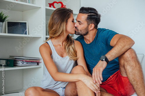Woman and man are sitting on the bed and kissing. Home backgroun