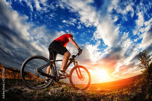 cyclist standing with mountain bike on trail at sunset