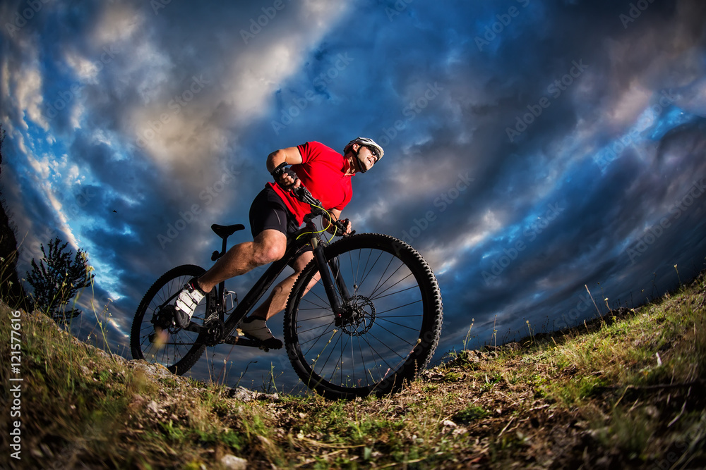 Naklejka premium cyclist standing with mountain bike on trail at sunset