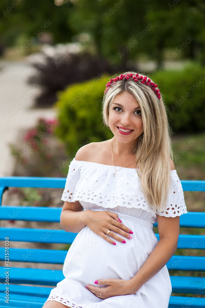 Naklejka premium Beautiful lovely girl wearing her first child in the stomach and is looking forward to his birth. Strolling in the park, enjoy nature and quietness