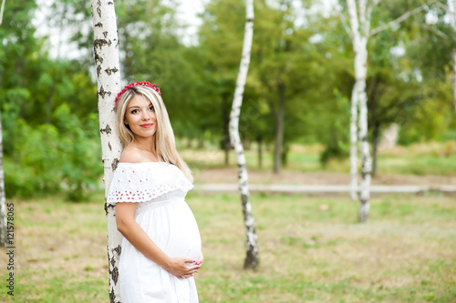 Beautiful lovely girl wearing her first child in the stomach and is looking forward to his birth. Strolling in the park, enjoy nature and quietness