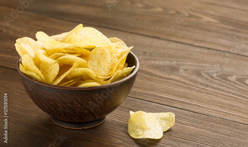 Potato chips in a bowl on wooden table.