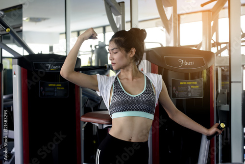 Happy sporty fitness woman flexing muscles in public fitness gym.