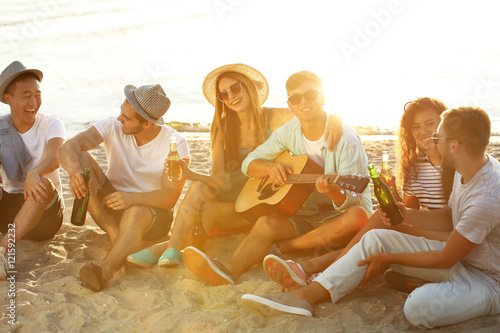 Group of friends listening to guitar and drinking beer at beach © Africa Studio