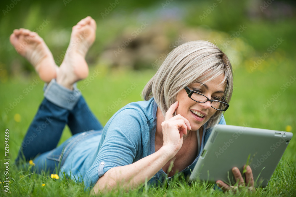 a nice retired woman reading on her tablet in the garden a nice retired woman reading on her tablet in the garden