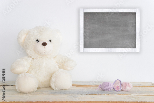 A teddy bear on a wooden table next to some handmade amigurumi figures. A blackboard with empty copy space for Author's text.