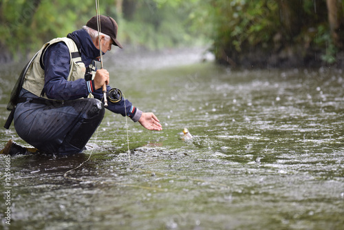 Fly-fisherman catching trout in river, under the rain