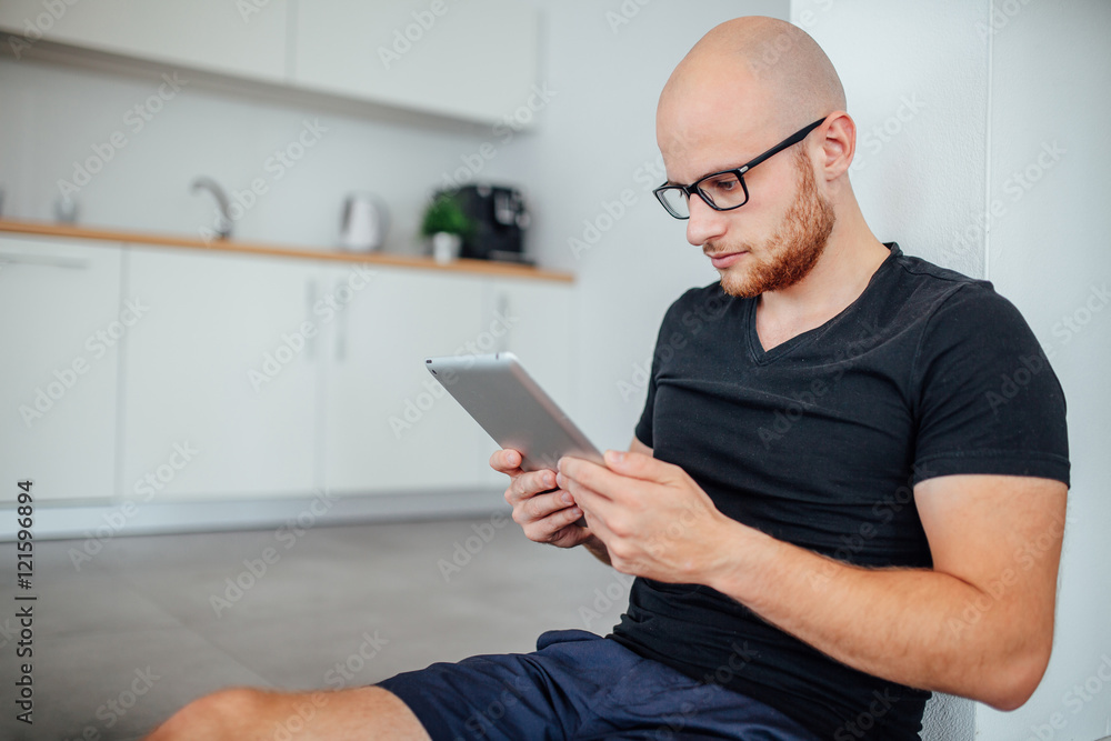 Man is sitting and using tablet pc. Kitchen background Man is sitting and using tablet pc. Kitchen background