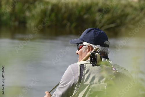 Fly-fisherman waiting with fishing pole on shoulder