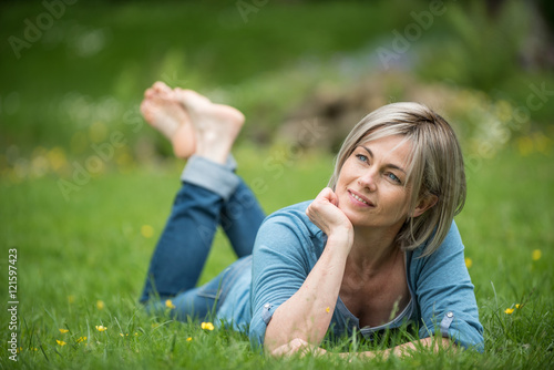  a woman of 45 years lying in grass in park. she is dreaming