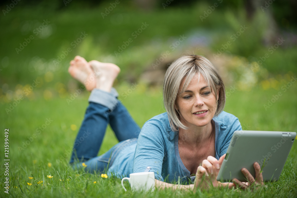 a woman lying in the grass with her tablet and a cup of tea a woman lying in the grass with her tablet and a cup of tea