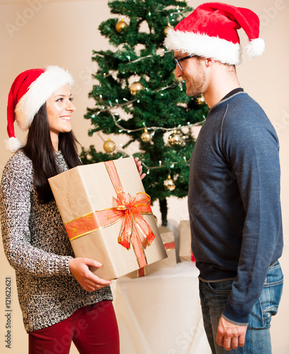 A young couple standing in front of the Christmas tree and givin photo