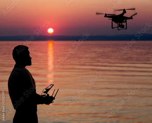 Man flying a drone near seaside at the sunset.