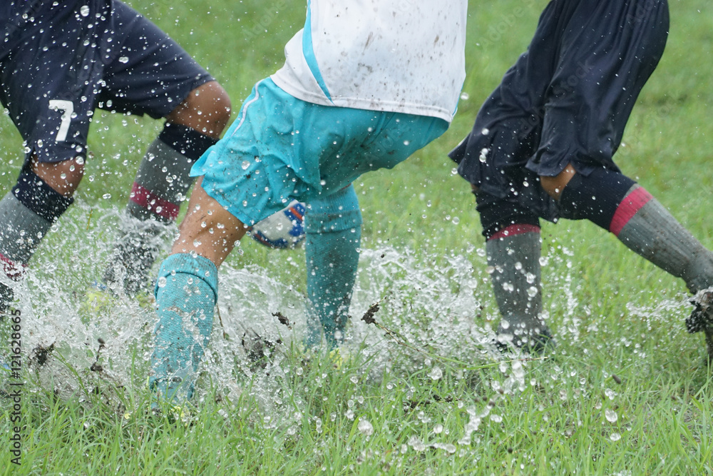 Young girls playing soccer in the rain on a wet grassy field Stock