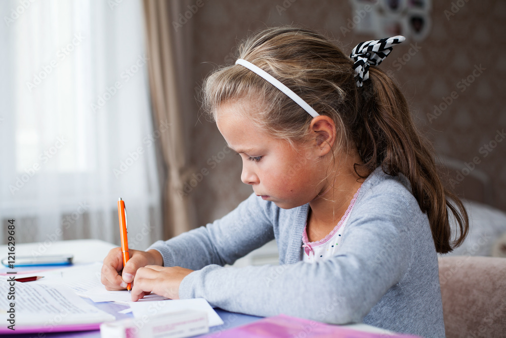 Serious little school girl doing homework, sitting with a pencil at the table Serious little school girl doing homework, sitting with a pencil at the table