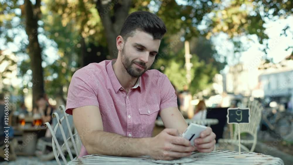 Handsome man using smartphone in the outdoor cafe and smiling to the camera
Handsome man using smartphone in the outdoor cafe and smiling to the camera