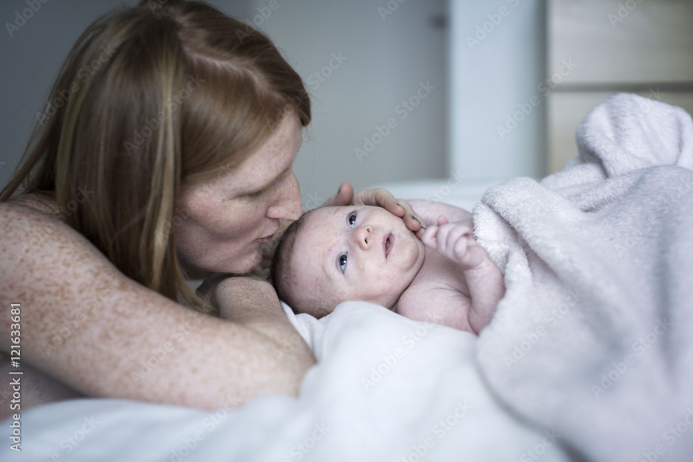 Mother touching her newborn baby lying on bed Mother touching her newborn baby lying on bed