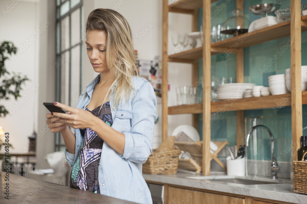 Young woman standing in kitchen with cell phone Young woman standing in kitchen with cell phone
