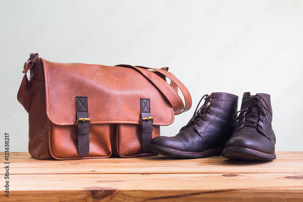 Men's fashion with brown leather bag and brown boots on wooden table over wall background