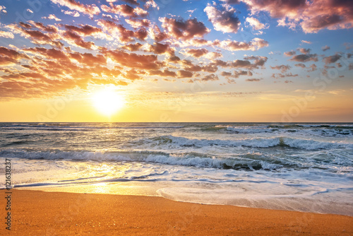 Colorful ocean beach sunrise with deep blue sky and sun rays.