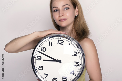 Beautiful young woman looking at a large silver retro clock that she is holding, she wonders how much time passed