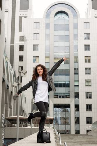 Glamorous young brunette woman in black leather jacket posing and having fun in the city street.