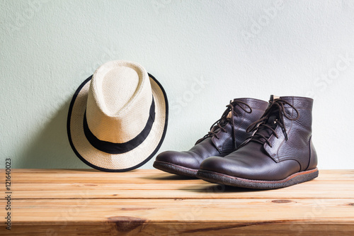 Men's fashion with brown boots and hat on wooden table over wall background
