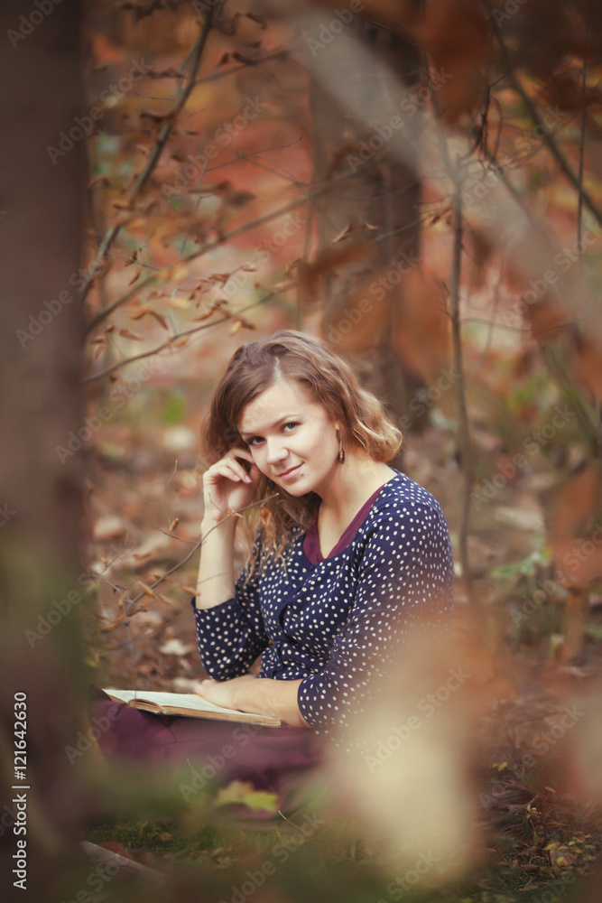 Beautiful young brunette sitting on a fallen autumn leaves in a park, reading a book Beautiful young brunette sitting on a fallen autumn leaves in a park, reading a book