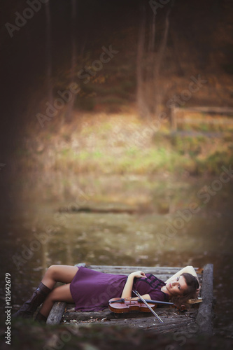 woman lying on a wooden pier near autumn forest lake with violin musical notes and books.