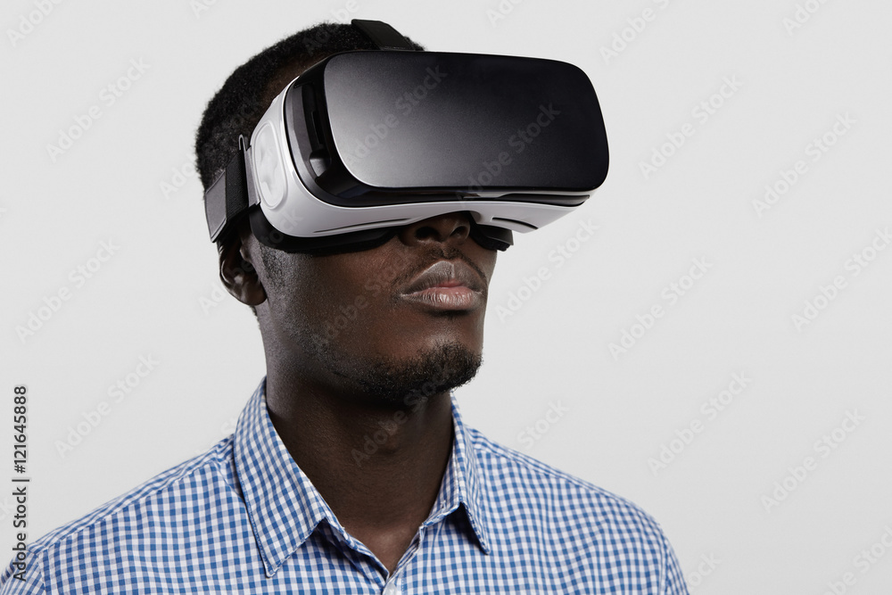 Technology, entertainment, gaming, cyberspace and people concept. Serious dark-skinned player wearing checkered shirt and big modern 3-D glasses. Black man playing video game with VR headset Technology, entertainment, gaming, cyberspace and people concept. Serious dark-skinned player wearing checkered shirt and big modern 3-D glasses. Black man playing video game with VR headset