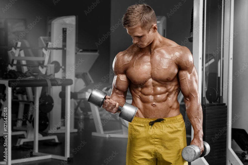 Muscular man working out in gym doing exercises with dumbbells at biceps, strong male naked torso abs