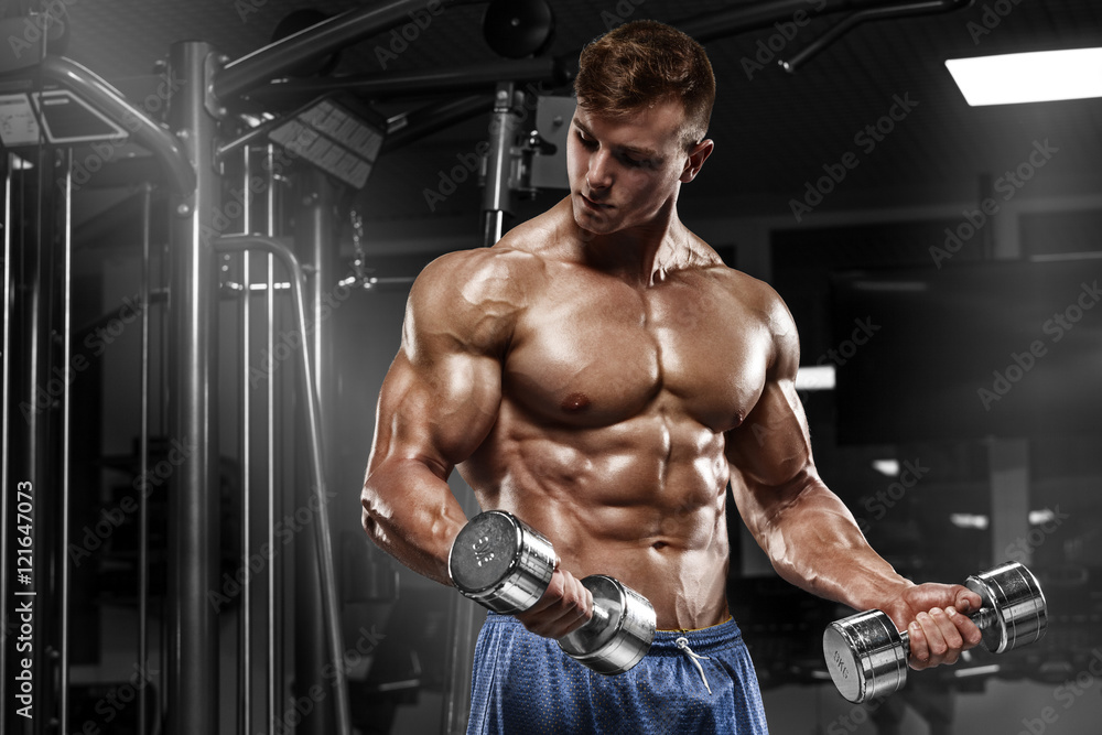 Muscular man working out in gym doing exercises with dumbbells at biceps, strong male naked torso abs Muscular man working out in gym doing exercises with dumbbells at biceps, strong male naked torso abs