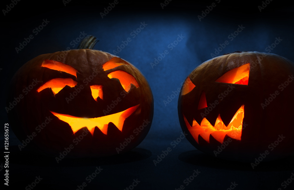 Fototapeta premium Two carved faces of pumpkins glowing on Halloween on blue background
