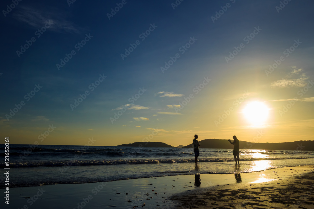 Silhouette of young take photo on sunrise beach.