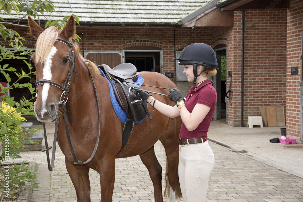Young rider preparing a pony for her riding lesson - September 2016 - Teenager adjusting the stirrup length Young rider preparing a pony for her riding lesson - September 2016 - Teenager adjusting the stirrup length