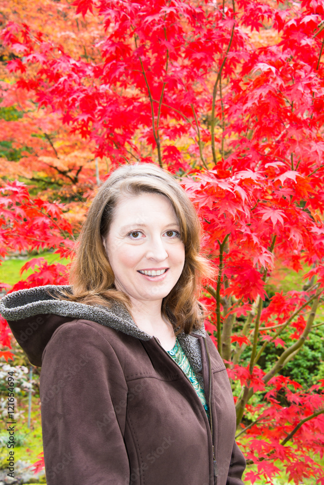 Autumn Portrait of Smiling Woman with Blurred Red Maple Tree in Background. Vertical. Copy Space. Autumn Portrait of Smiling Woman with Blurred Red Maple Tree in Background. Vertical. Copy Space.