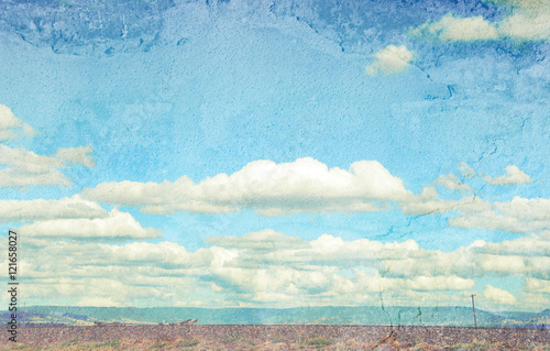 Rural cloudscape with flat road and power lines in foreground and mountain range in background. Faded and textured image with copy space.
