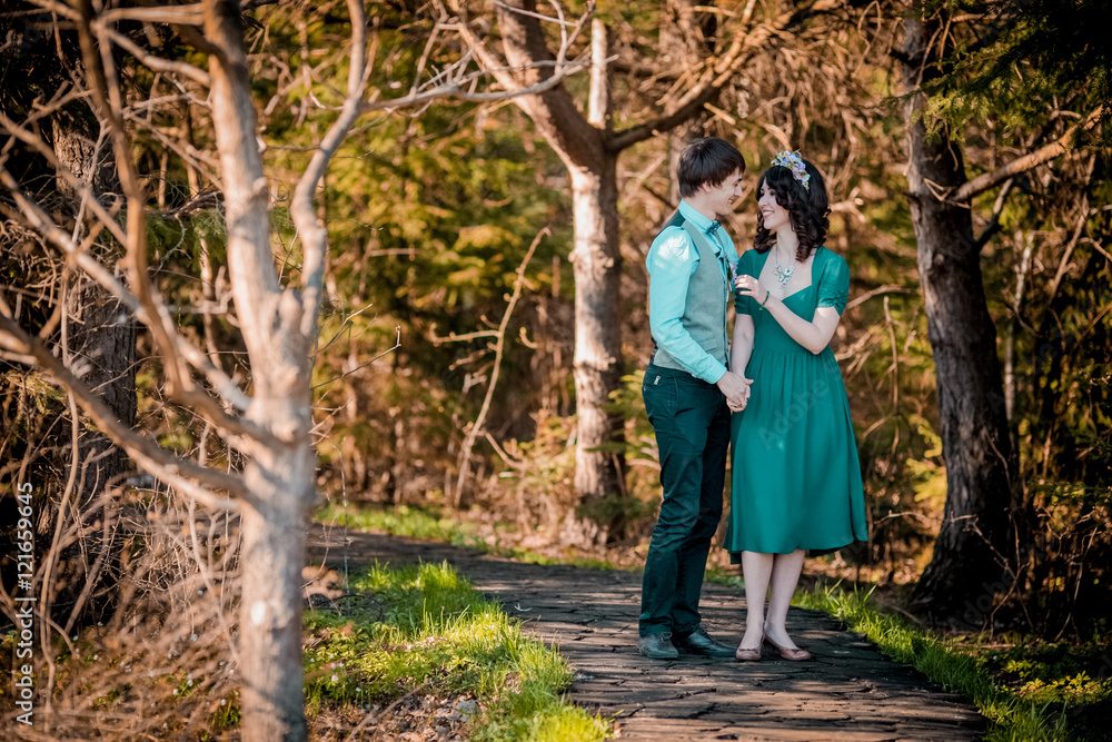 Lovers walking hand in hand in autumn park. Woman in green dress and wreath. Man in blue shirt and gray waistcoat Lovers walking hand in hand in autumn park. Woman in green dress and wreath. Man in blue shirt and gray waistcoat